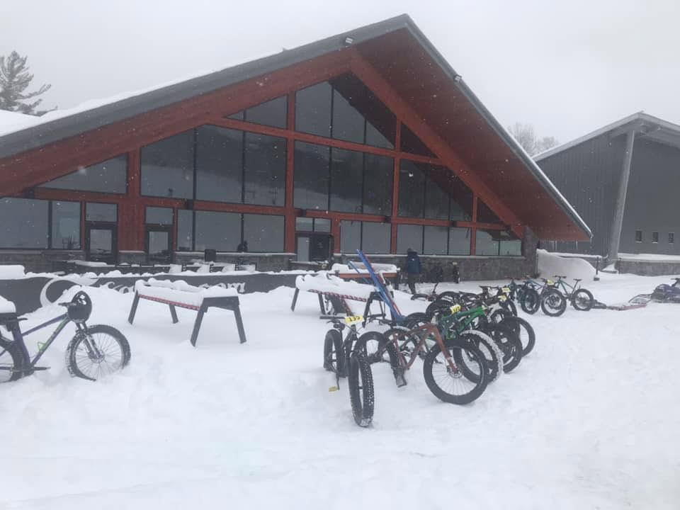 Fat bikes lined up in falling snow outside a lodge on a winter ride day