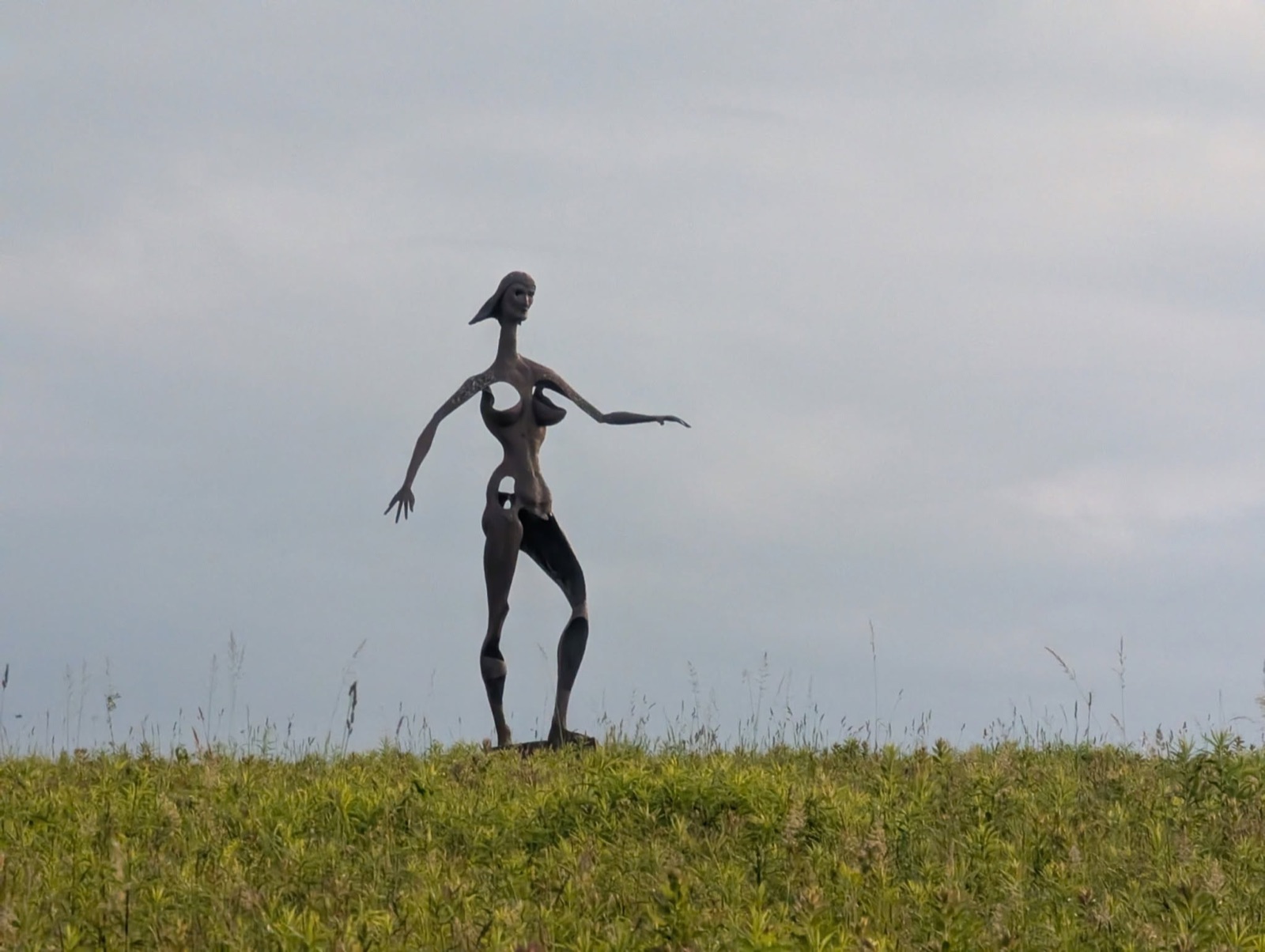 Tall metal figure sculpture standing alone on a grassy hilltop at Griffis Sculpture Park
